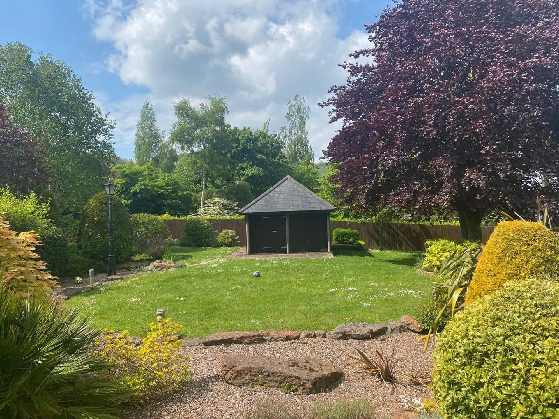 Before the garden re-design - a flat area of lawn with small building, and mature trees and bushes