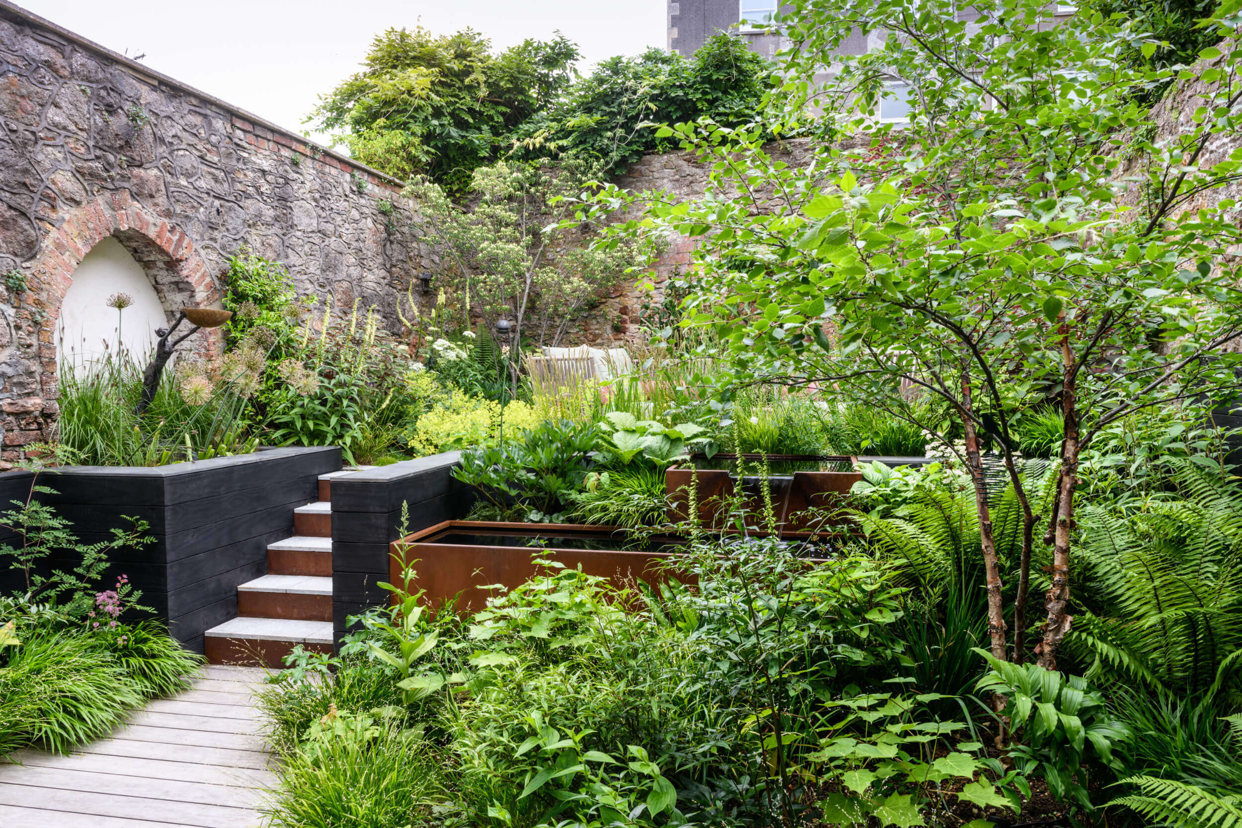 Lush green planting in the fore, with steps up to the second level of a courtyard garden.